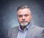Studio portrait of a mature man with a beard and gray suit against a textured gray background.